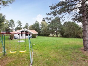 A residential property with a grassy yard, a swing set, and a house with a red roof.