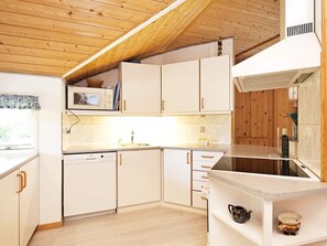 A modern kitchen with wooden ceiling beams, white cabinetry, and a built-in dishwasher.