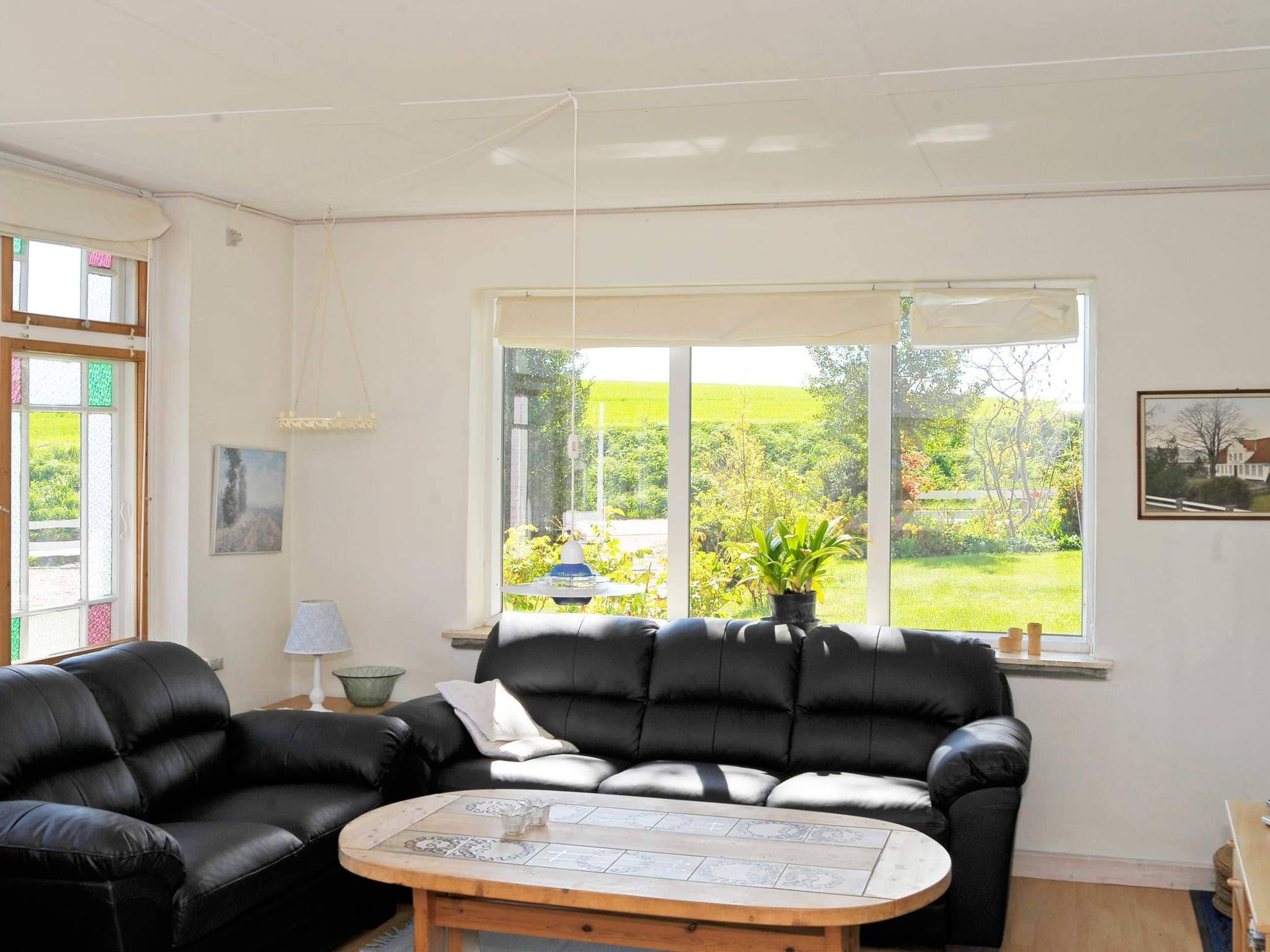Una sala de estar con un sofá de cuero negro, una mesa de centro redonda de madera y un ventanal con vistas a zonas verdes.