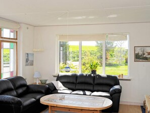 A living room with a black leather sofa, a round wooden coffee table, and a large window with a view of greenery. - Peaceful Holiday Home in Thisted near Sea (Nordborg)