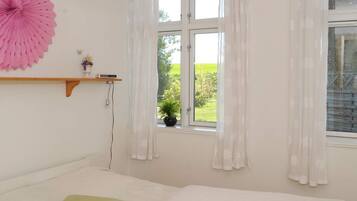 Ein Schlafzimmer mit einem Bett, einem Fenster mit Vorhängen, einem an der Wand befestigten Regal mit einer Pflanze und einem großen, dekorativen Fächer.