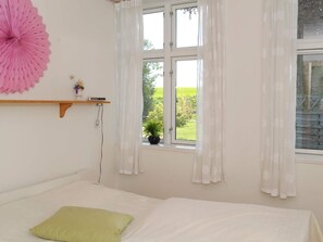 A bedroom with a bed, a window with curtains, a wall-mounted shelf with a plant, and a large decorative paper fan. - Peaceful Holiday Home in Thisted near Sea (Nordborg)