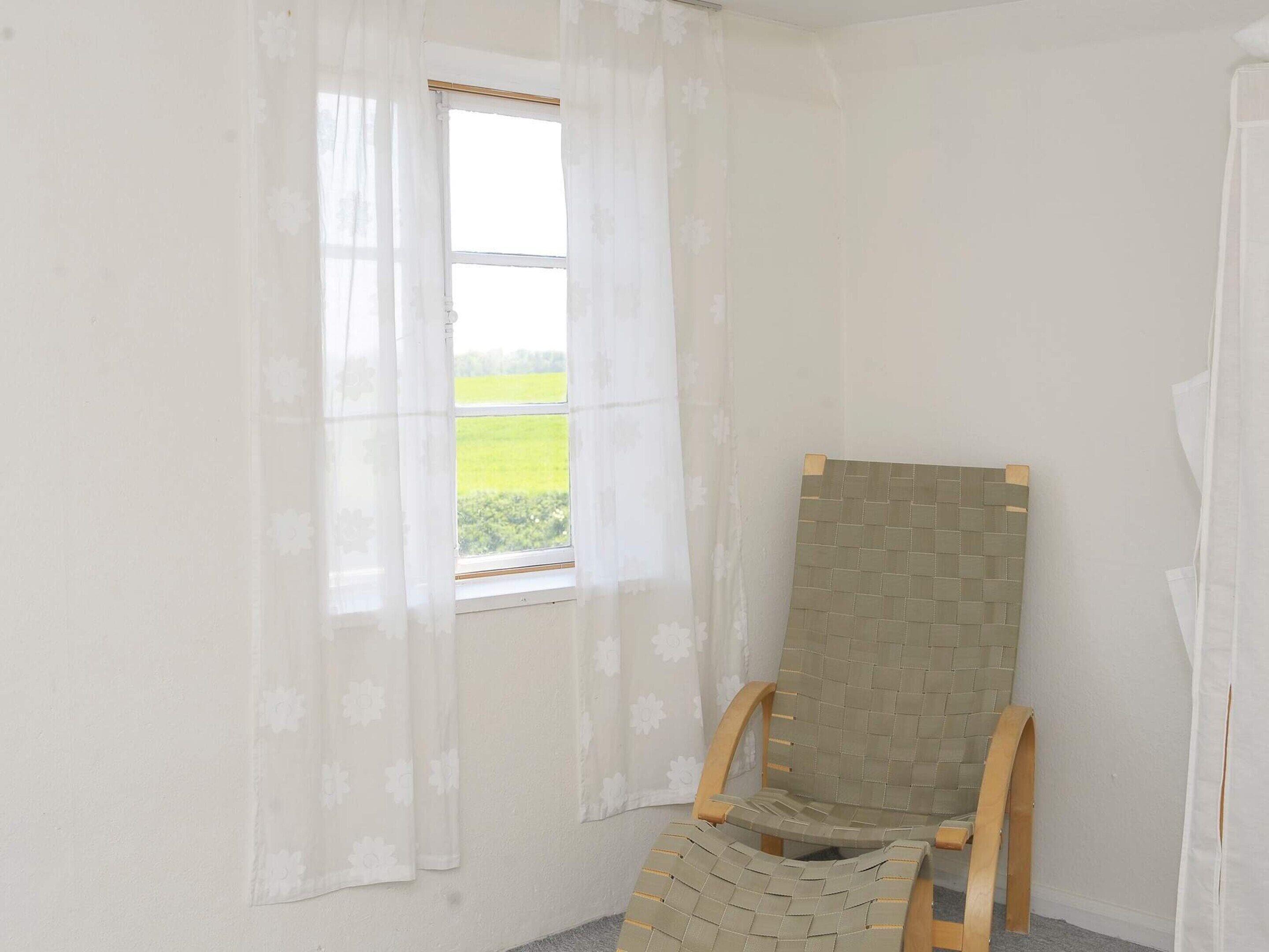 A room with a window, a wooden chair, and a wall-mounted item.