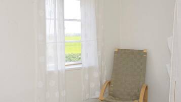 A room with a window, a wooden chair, and a wall-mounted item.