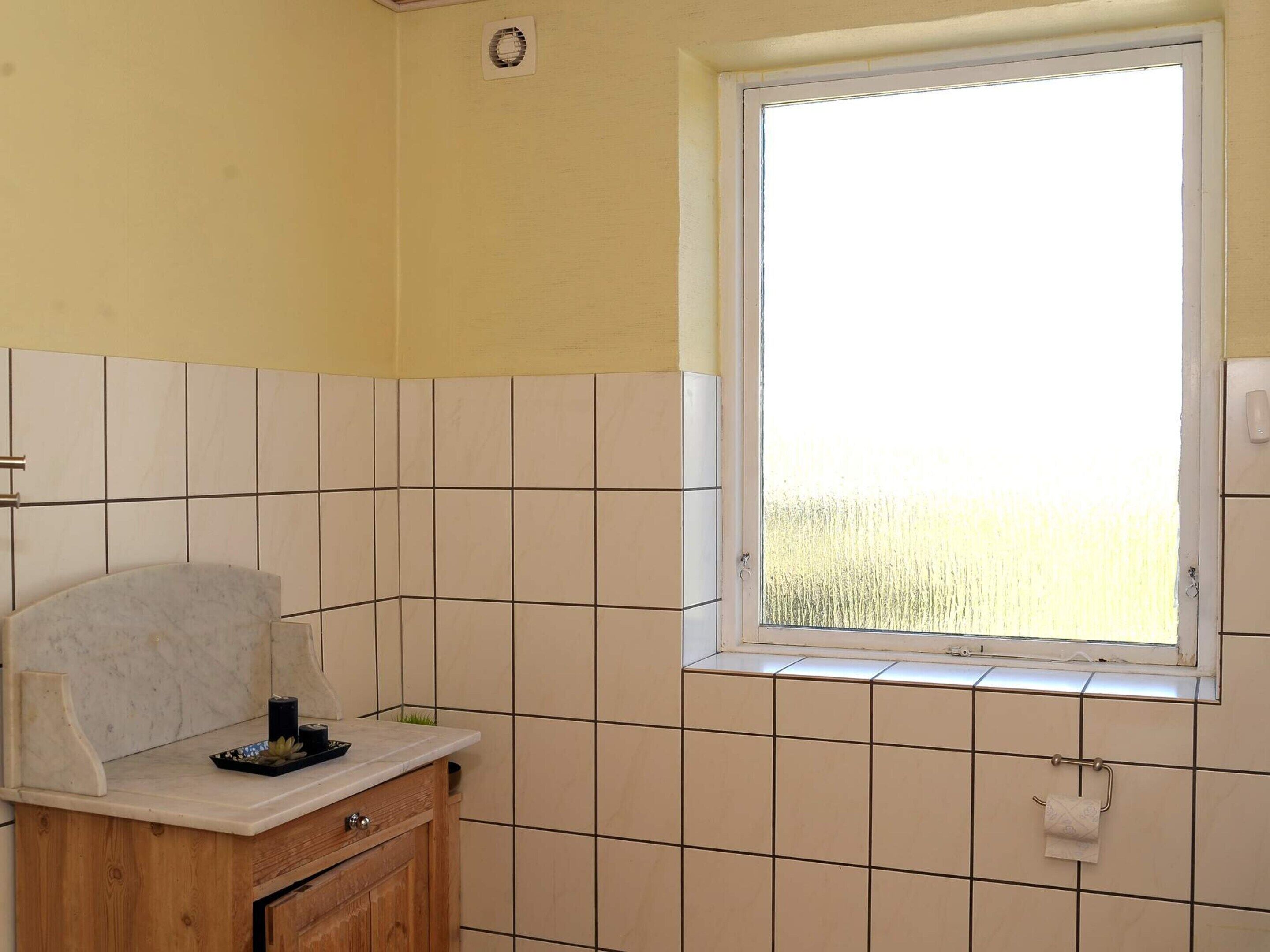 Ein Badezimmer mit Fenster, Waschbecken inklusive Spiegel und Toilette.