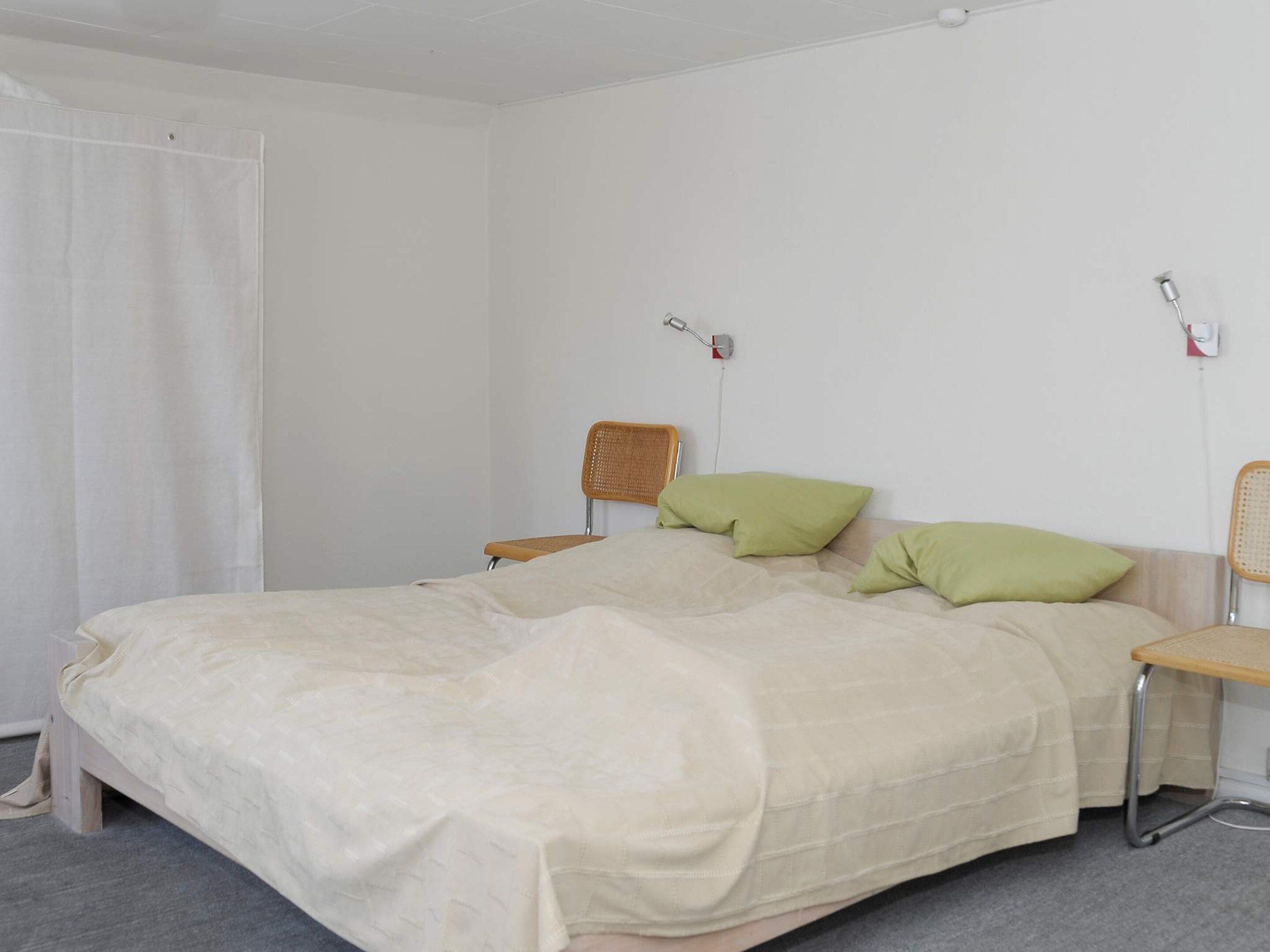 Un dormitorio con una cama, dos almohadas, una silla y una mesita de noche.