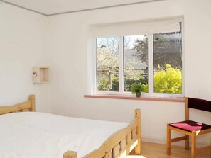 A bedroom with a wooden bed, a chair, a small shelf, and a window with a view of greenery. - Peaceful Holiday Home in Thisted near Sea (Nordborg)