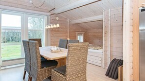 Ein gemütliches Holzhaus mit Essbereich, der Korbstühle und einen Holztisch bietet, einem Bett mit Aussicht und einem eingebauten Kühlschrank.