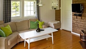 A living room with a beige sofa, green pillows, a white coffee table, a wooden floor, a white door, and a mounted television. - 4 Person Holiday Home in Utvik (Stryn)