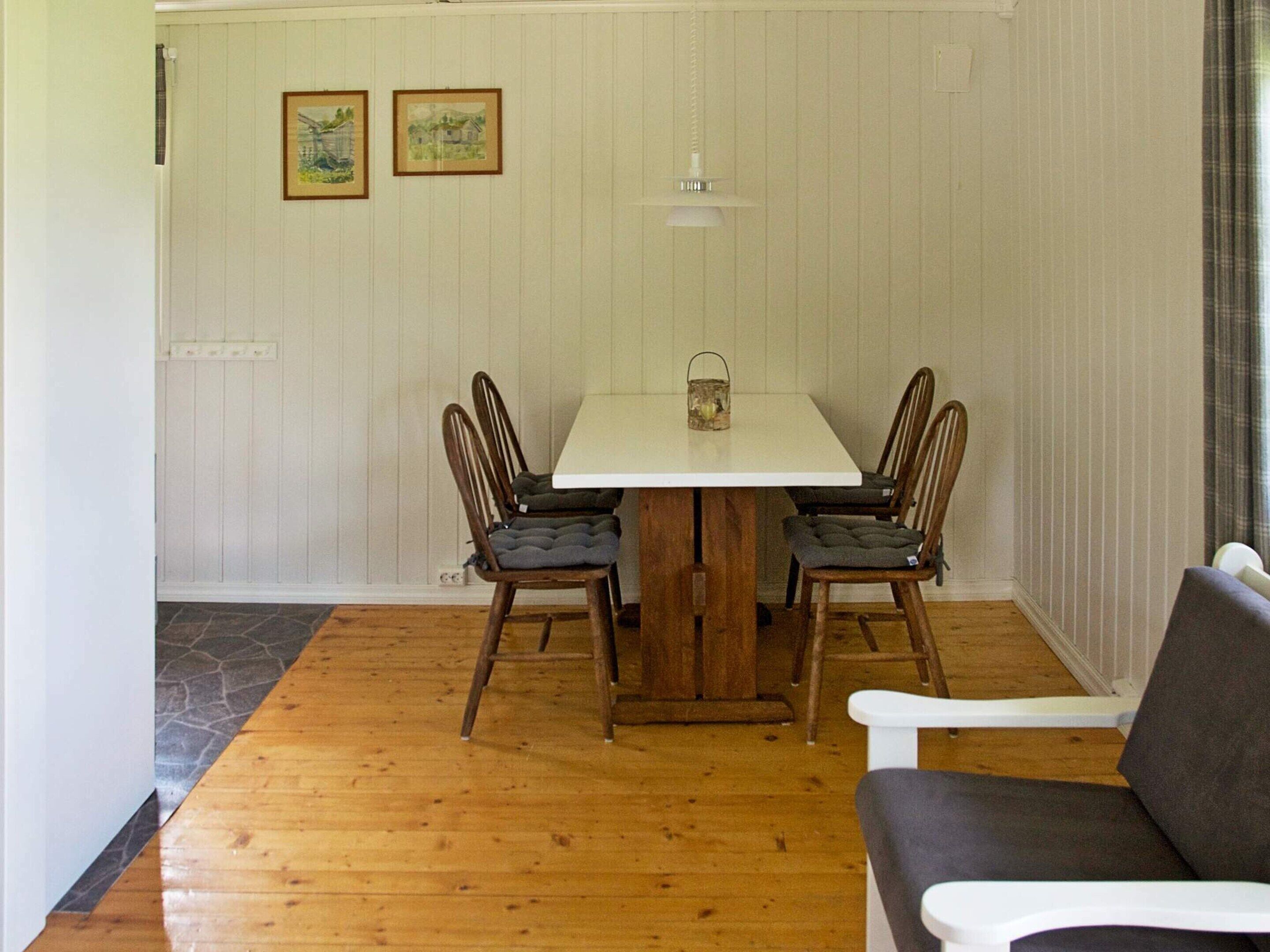 A dining area with a wooden table and four chairs, a small lamp, and two framed pictures on the wall.
