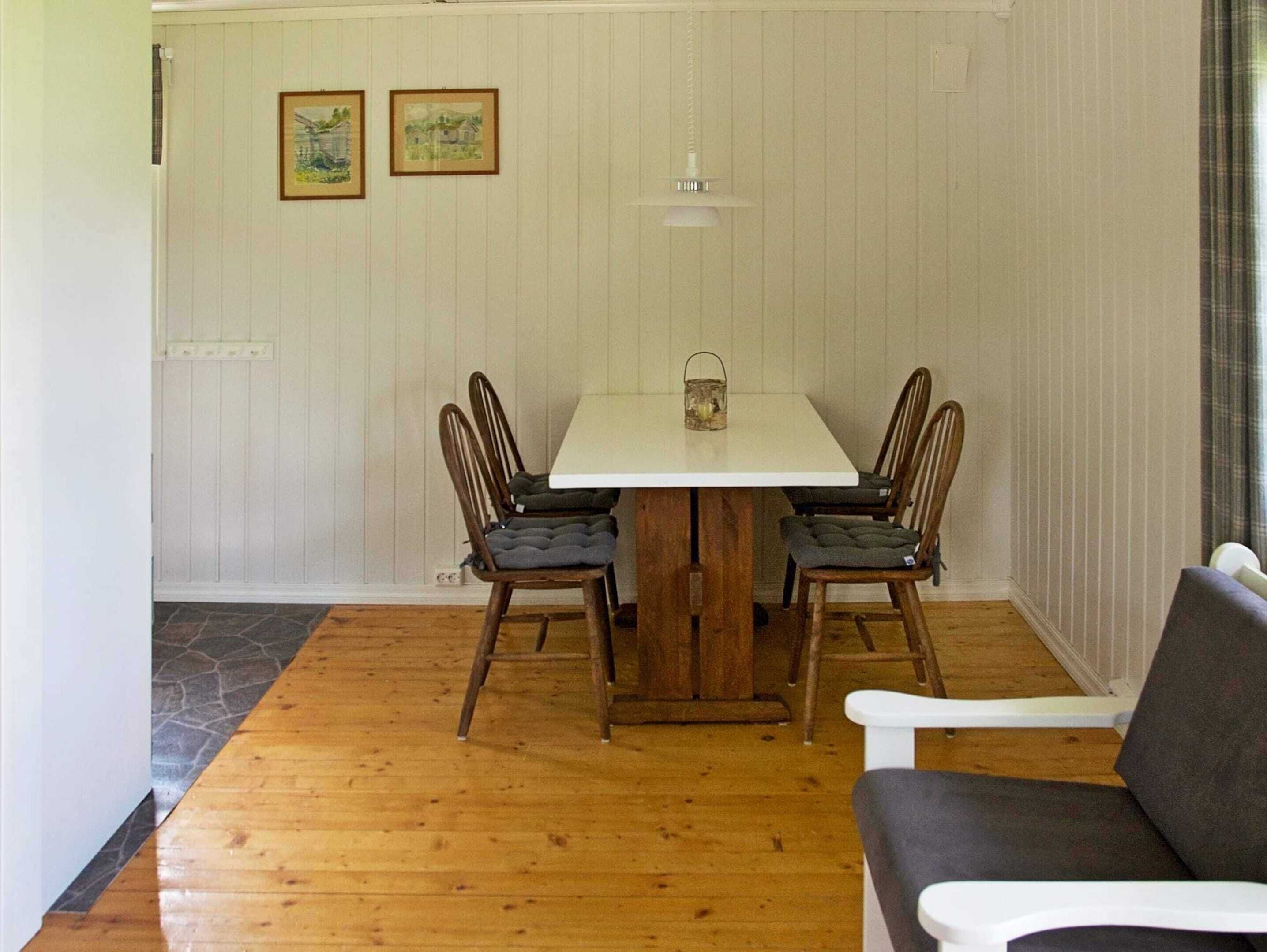 Un comedor con una mesa blanca, sillas de madera y una pequeña lámpara colgante.