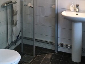 Une salle de bain comprenant des toilettes, une douche avec une porte en verre et un lavabo avec un distributeur de savon.