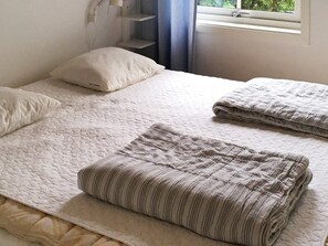 Un lit recouvert d’une couette blanche matelassée, un oreiller et deux couvertures pliées.