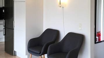 Ett modernt kök med ett svart kylskåp, två mörka fåtöljer och en väggmonterad lampa.