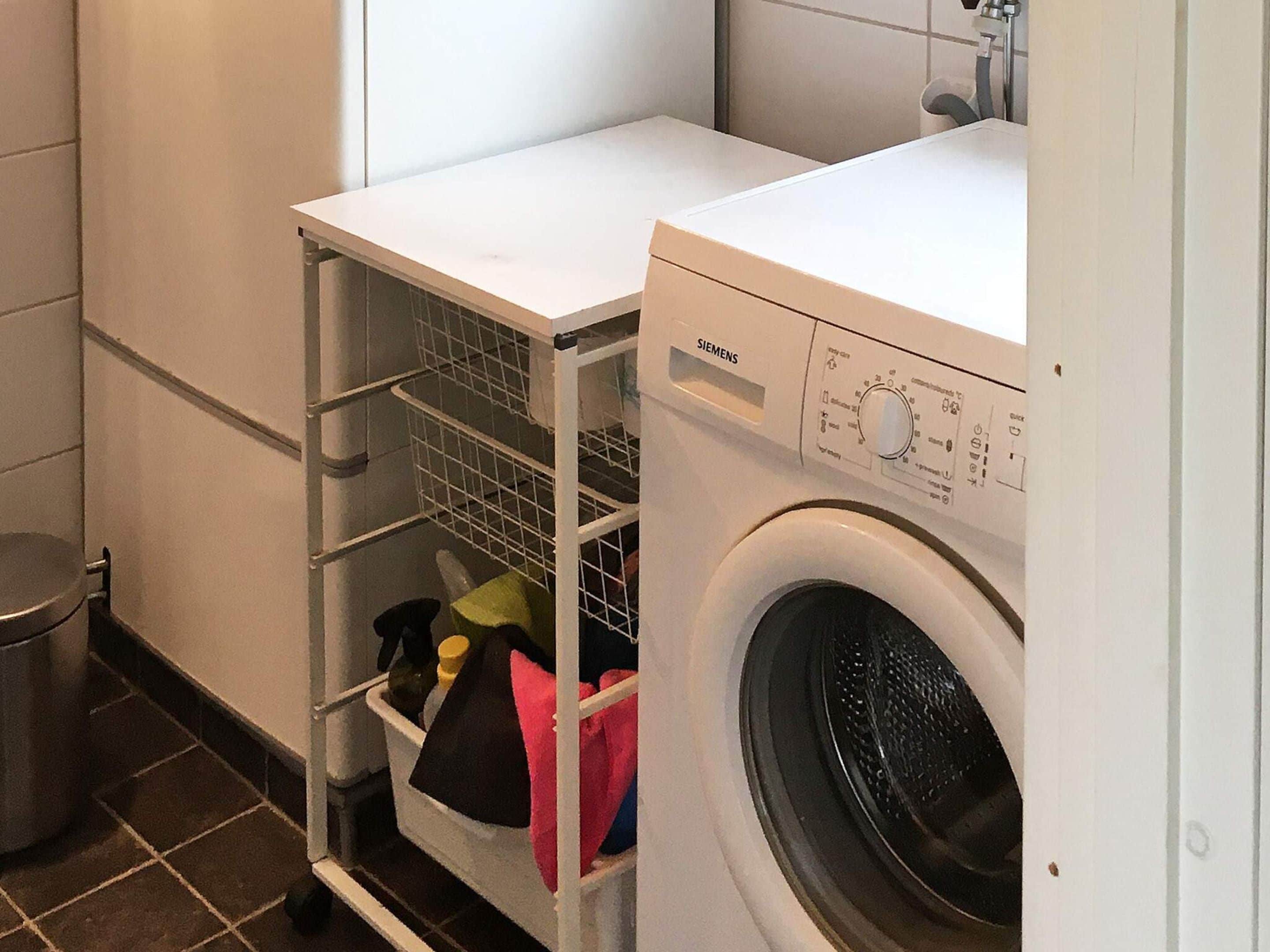 Ett kompakt tvättrum med en tvättmaskin från Siemens och en hyllsektion i metall för förvaring.
