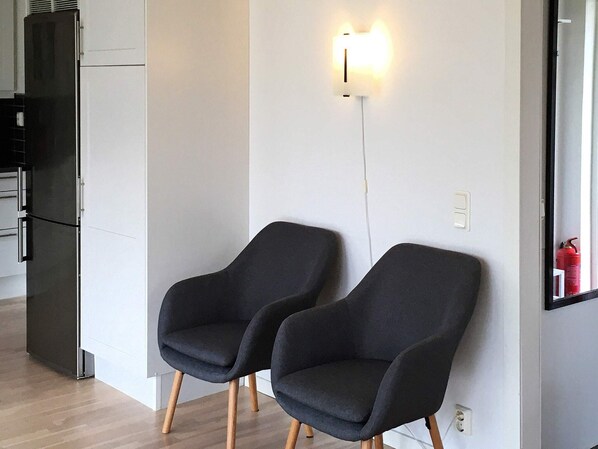 Une cuisine moderne avec un réfrigérateur noir, deux fauteuils sombres et un luminaire fixé au mur.