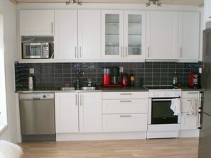 Une cuisine avec des meubles blancs, un four à micro-ondes, une machine à café et une cuisinière.