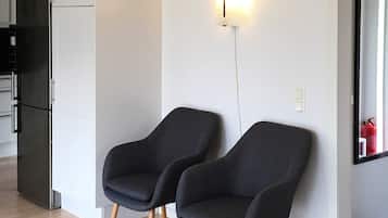 Ett modernt kök med ett svart kylskåp, två mörka fåtöljer och en väggmonterad lampa.