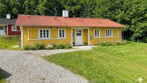 Une maison jaune avec un toit rouge, une allée en gravier et une pelouse verdoyante.