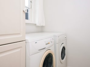 A compact laundry area with a front-loading washing machine and dryer, a small window with a curtain, and a white door. - 4 Star Holiday Home in Aabenraa (Aabenraa)