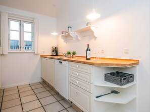 A kitchen with white cabinets, a wooden countertop, a coffee maker, a wine bottle, and a window with curtains. - 4 Star Holiday Home in Aabenraa (Aabenraa)