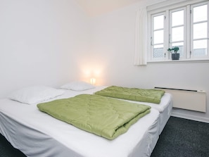 Quarto com duas camas, janela com vista e radiador fixado na parede.
