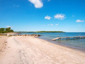 A sandy beach with a wooden pier extending into calm waters, surrounded by rocks and greenery. - 4 Star Holiday Home in Aabenraa (Aabenraa)