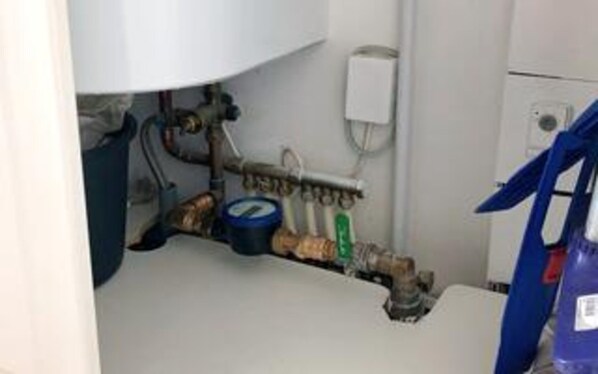 A bathroom with a sink, pipes, and a water heater.