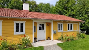 Une maison jaune avec un toit recouvert de tuiles rouges, des fenêtres blanches et une porte d’entrée.