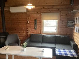 Un acogedor interior de cabaña de madera con un sofá, sillas, una mesita y una ventana con persianas.