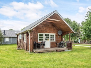 A log cabin with a porch, a dining table, and chairs.