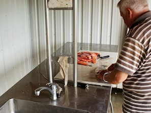 A man in a striped shirt working at a stainless steel counter with a knife and fish.
