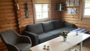 A cozy cabin interior with a grey sofa, a matching armchair, and a white table with decorative items.