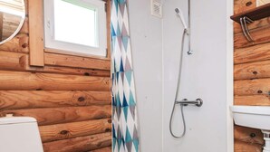 A wooden cabin bathroom with a shower, toilet, and a window.