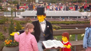 A LEGO sculpture of a man and a child in a park with a crowd in the background.