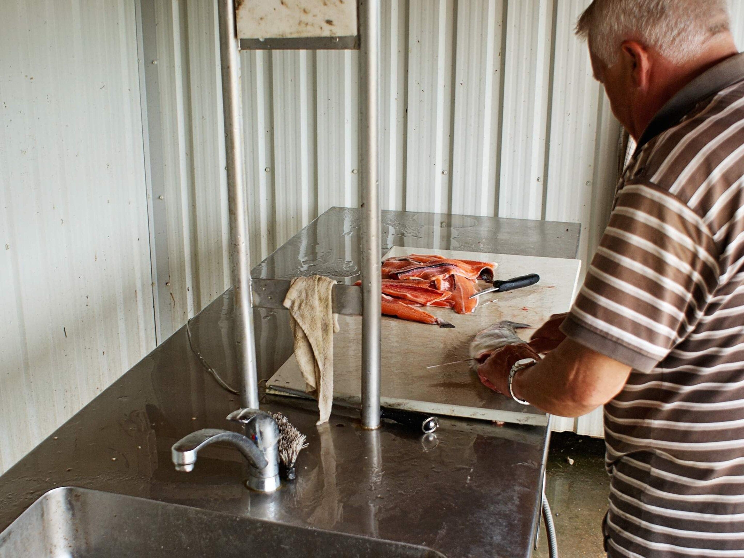 A person preparing food at a stainless steel counter with a sink and a cutting board.