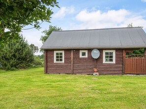 A log cabin with a satellite dish, a fenced yard, and a large tree to the left.