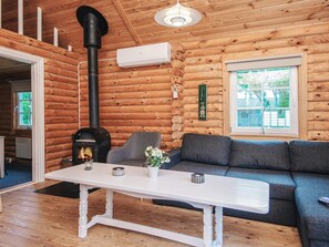 A cozy cabin interior with a fireplace, a sofa, a table, and a window with a view of greenery. - Cozy Holiday Home in Hovborg near Community Area (Hovborg)
