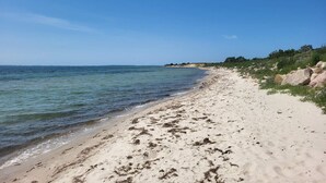En strand med klart vatten, sandstrand och klippiga utskjutande partier.