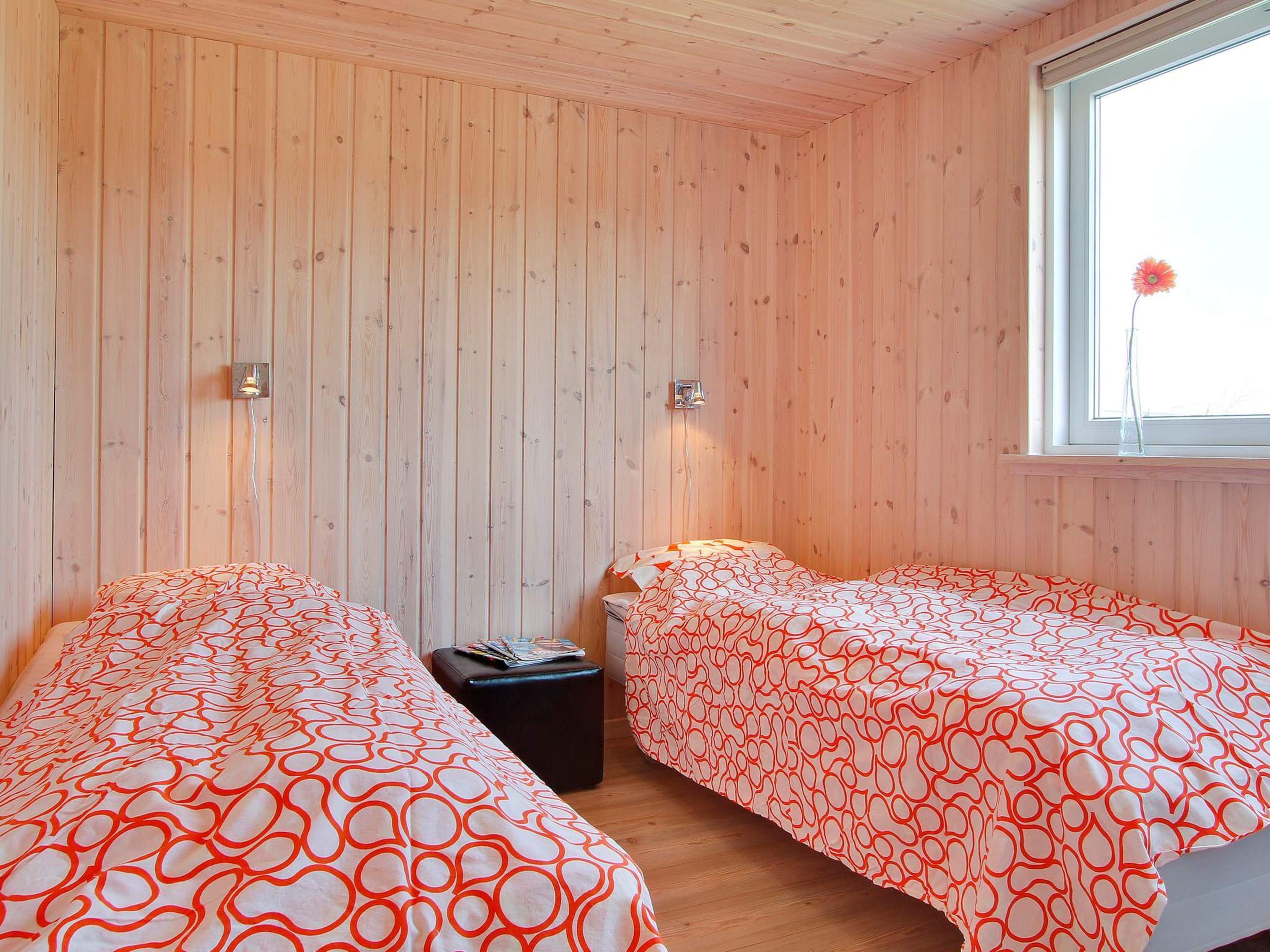 A room with two beds, wooden walls, a window with a flower, and two wall-mounted lights.