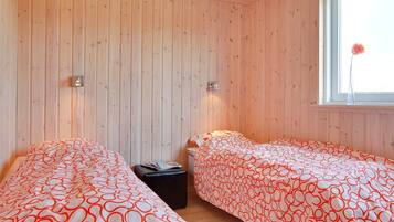 Een kamer met twee bedden, houten wanden, een raam met een bloem en twee wandlampen.
