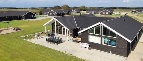 A modern residential building with a covered patio, outdoor seating, and a swimming pool.
