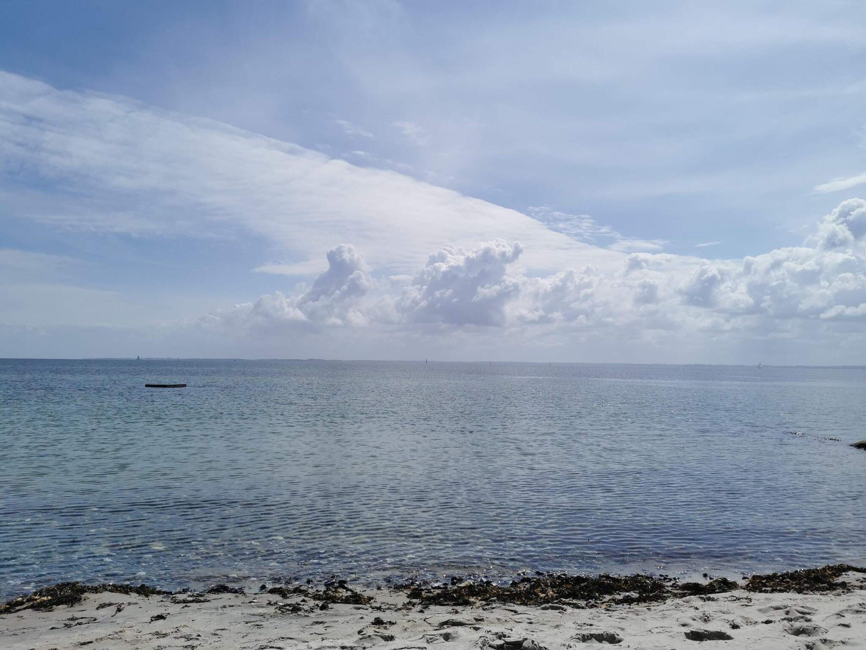 Ein Strand mit ruhigem Wasser, einem sandigen Ufer und weiter Küste im Hintergrund.