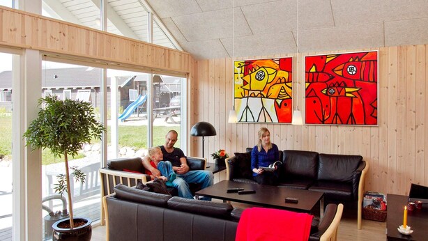 Ett modernt vardagsrum med en svart lädersoffa, ett träbord och ett stort fönster som ger utsikt över omgivningen.