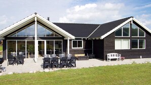 A two-story building with a large patio area, outdoor seating, and a covered section with glass doors. - 5 Star Holiday Home in Sydals (Sydals)