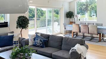 A modern living room with a grey sofa, a coffee table with remote controls, and a dining area with a table and chairs.