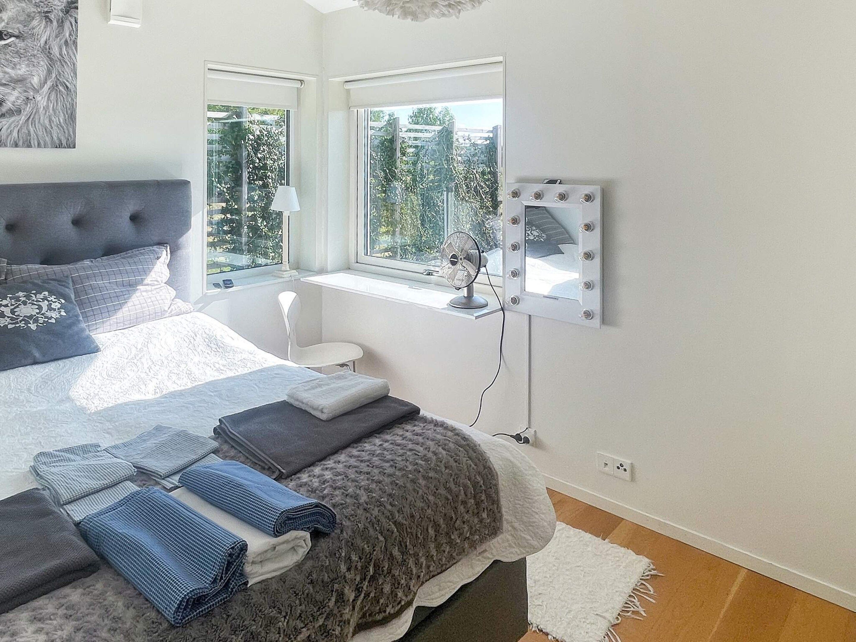 Ein Schlafzimmer mit Bett, Fenster, Schminktisch und einem Ventilator.