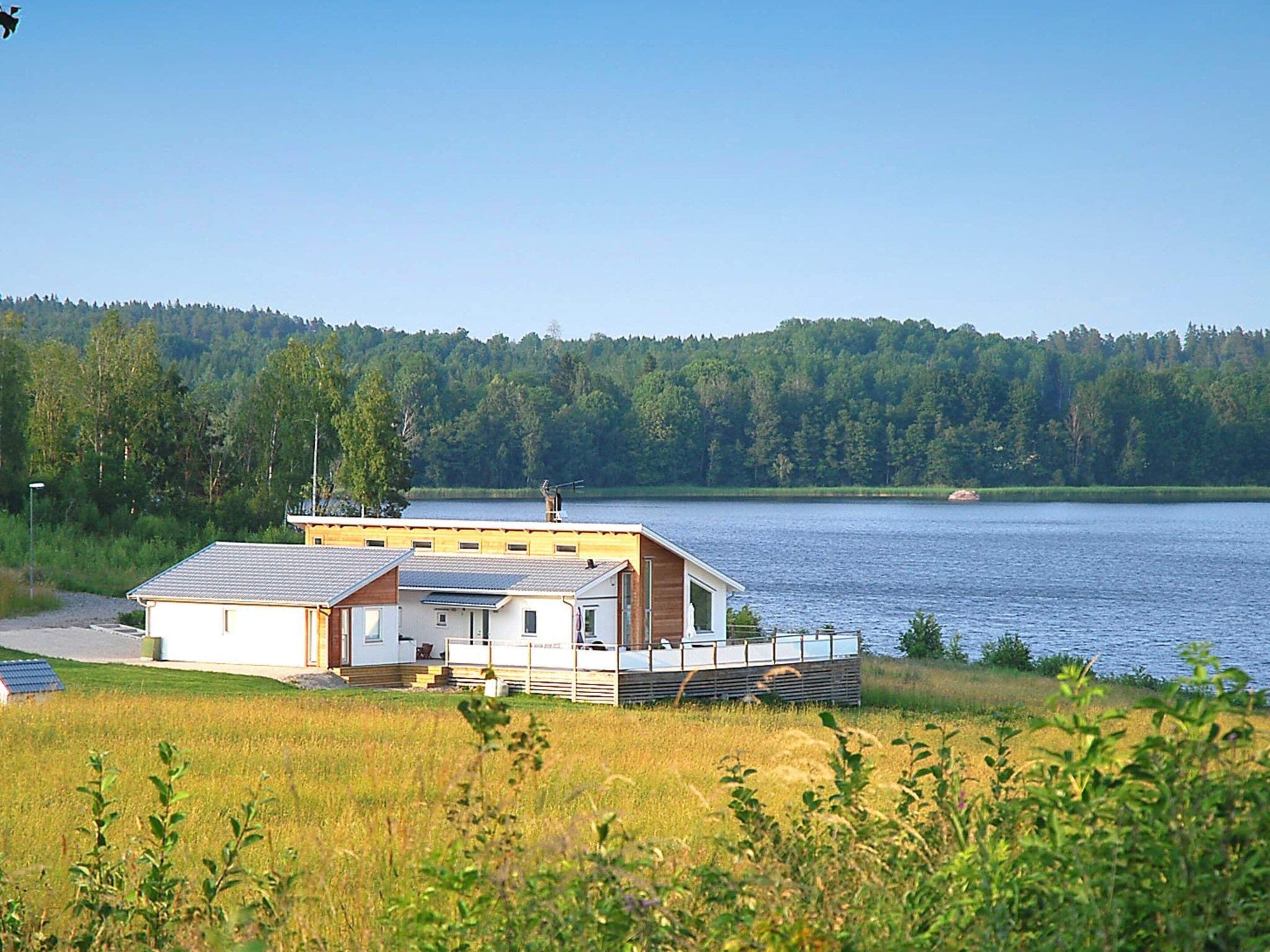 A lakeside cabin with a deck, surrounded by a forested area and a clear sky.