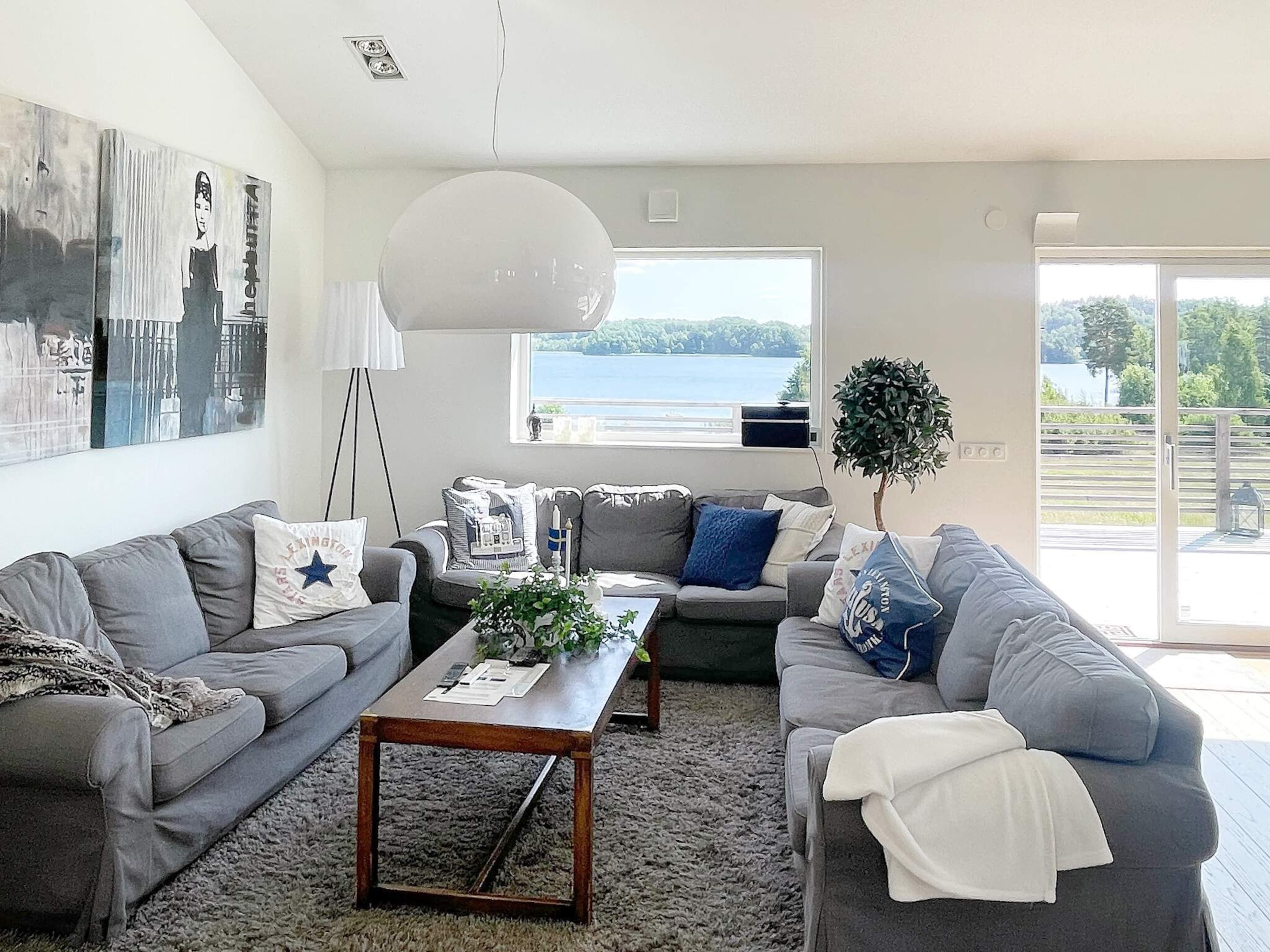 A modern living room with grey sofas, a wooden coffee table, and a large window with a view of a lake.