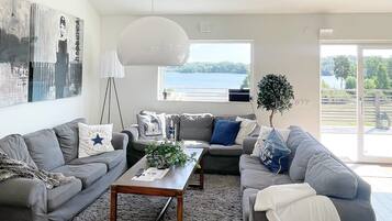 A modern living room with grey sofas, a wooden coffee table, and a large window with a view of a lake.